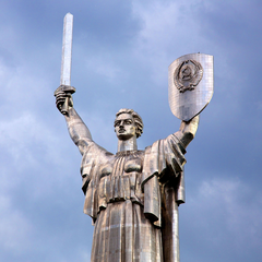 Жінка з українським прапором стоїть біля монументу