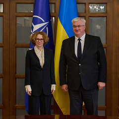 Дві жінки рукуються на фоні прапорів