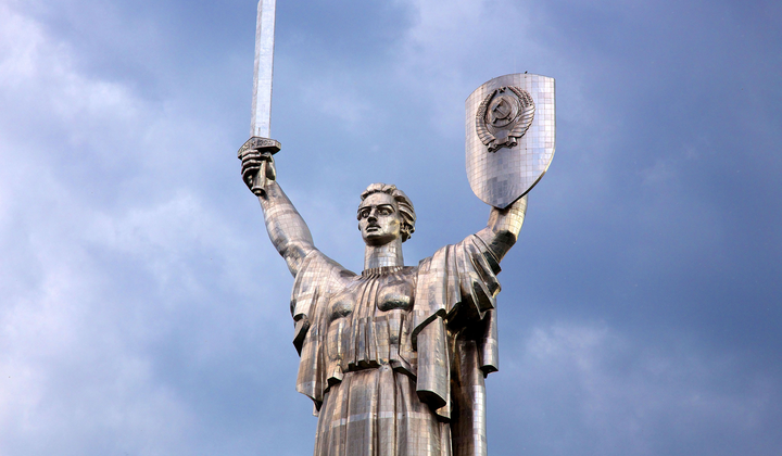 Жінка з українським прапором стоїть біля монументу