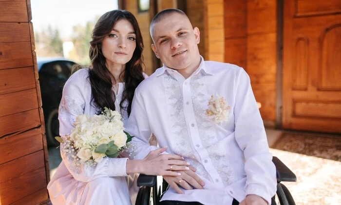 На зображенні дівчина, що тримає руку в руці військового хлопця у реанімаційному відділенні весело посміхаючись