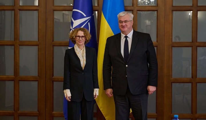 Дві жінки рукуються на фоні прапорів